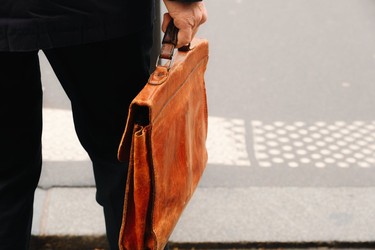 why-choose-us Close-up view of a vintage leather briefcase being held by a person's hand outdoors.