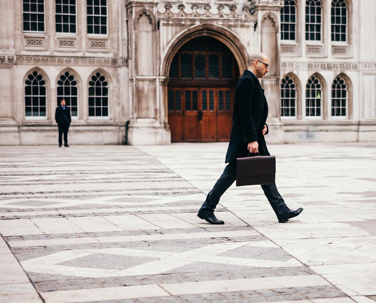A businessman in formal attire walking past a historic building facade.