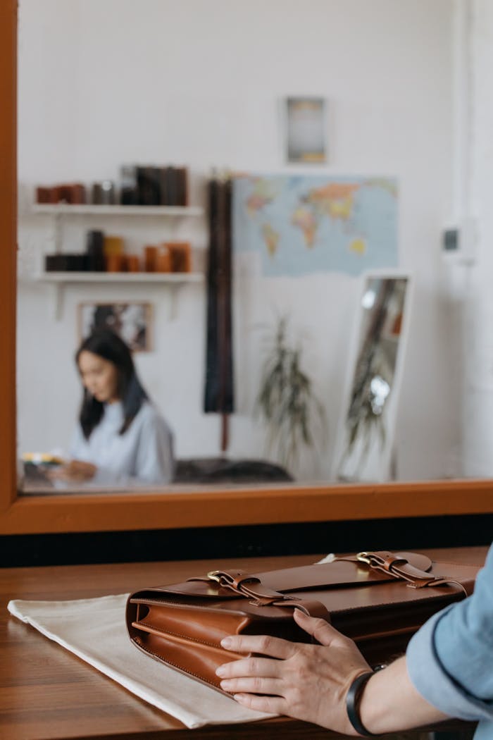 A brown leather briefcase on a desk in a stylish modern office setting with a blurred background.