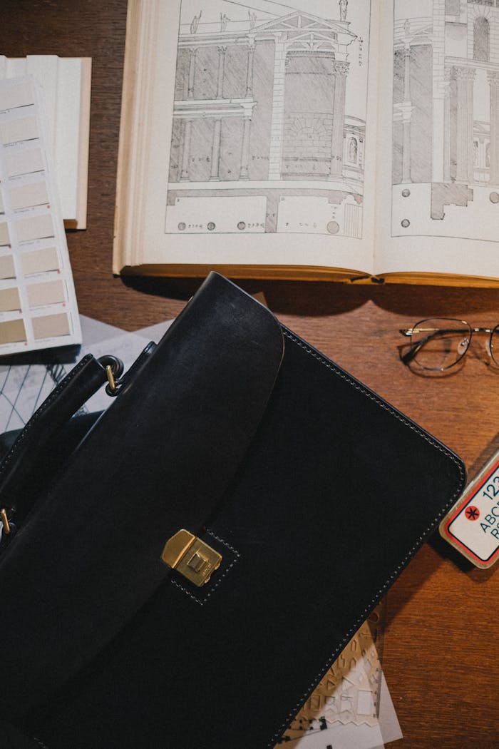 services-02 A top-down view of a study desk featuring a vintage architecture book, glasses, and a black leather briefcase.